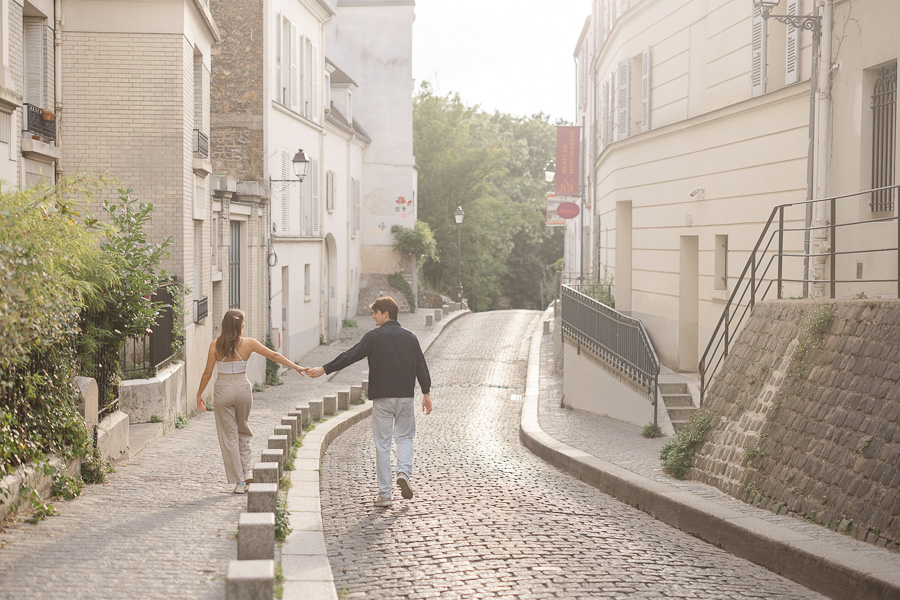 Couple walking hand in hand through golden light cobblestone street in Montmartre Paris
