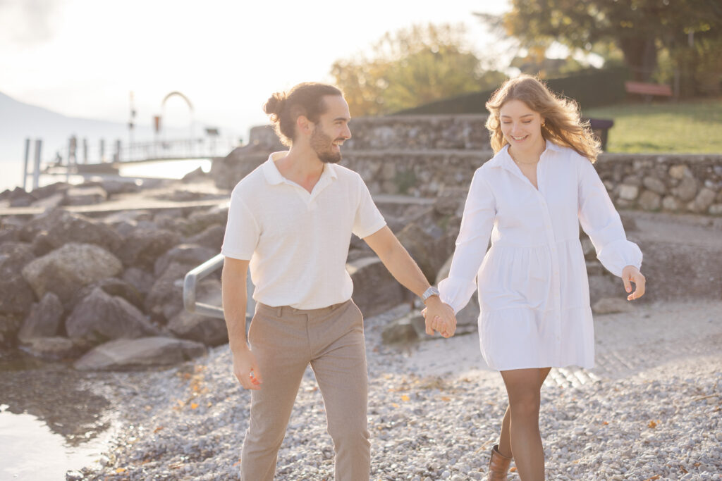 Couple walking hand in hand along Lake Geneva shore during engagement session