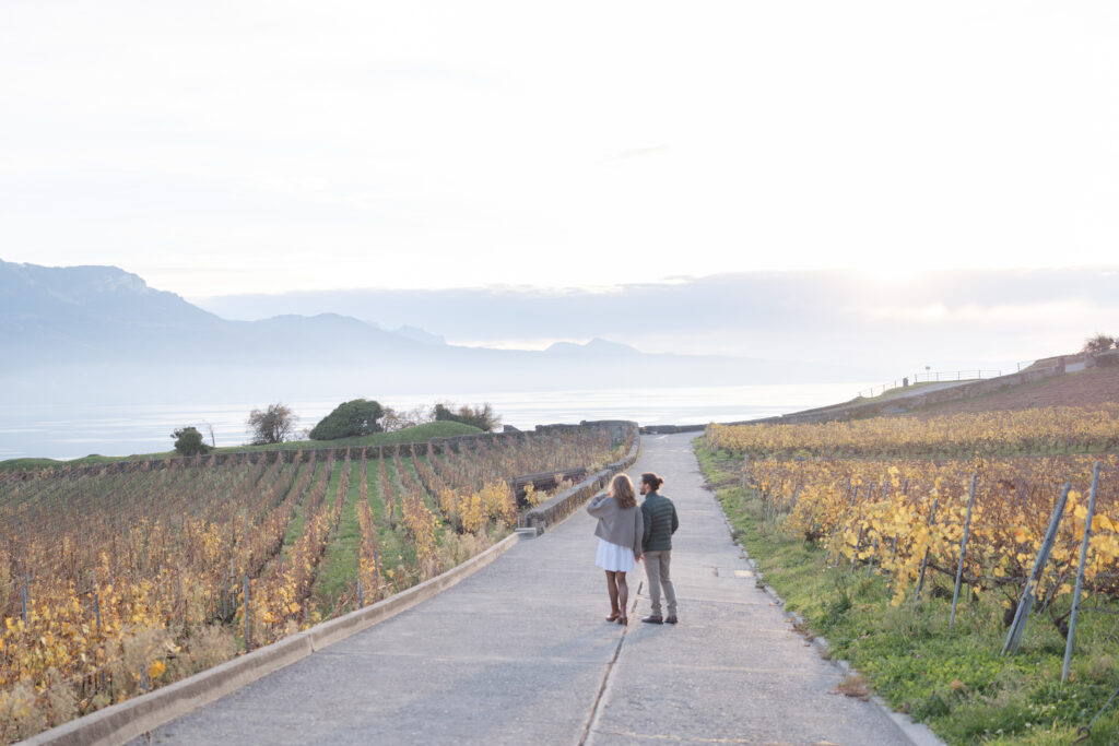 Couple walking along road through Lavaux golden vineyards during engagement session Switzerland