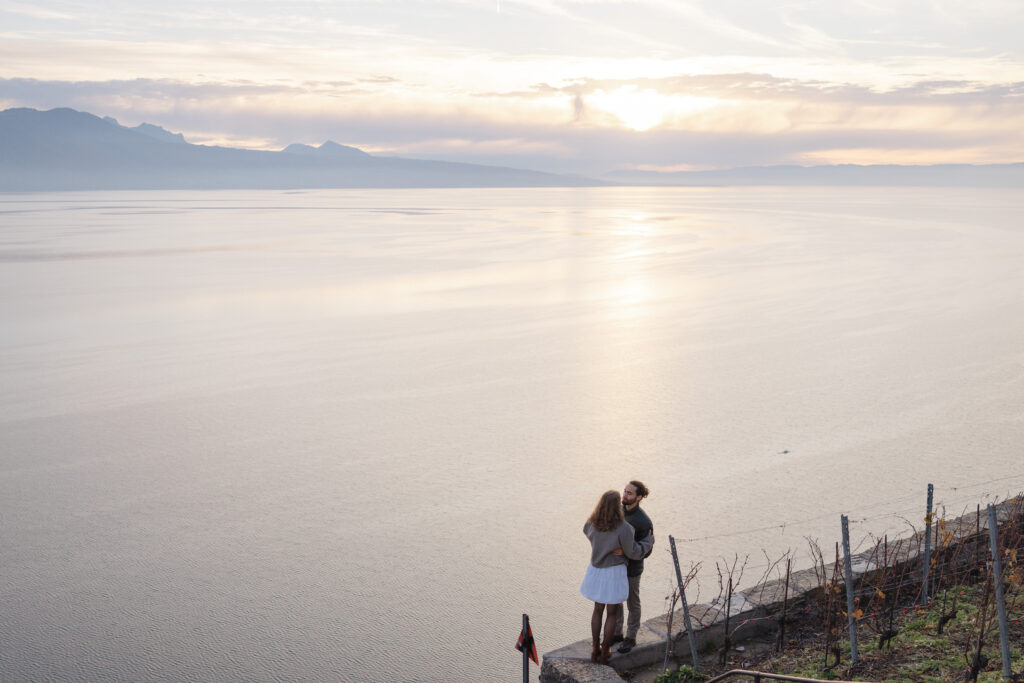 Couple embracing at sunset overlooking Lake Geneva during engagement session in Lavaux vineyards