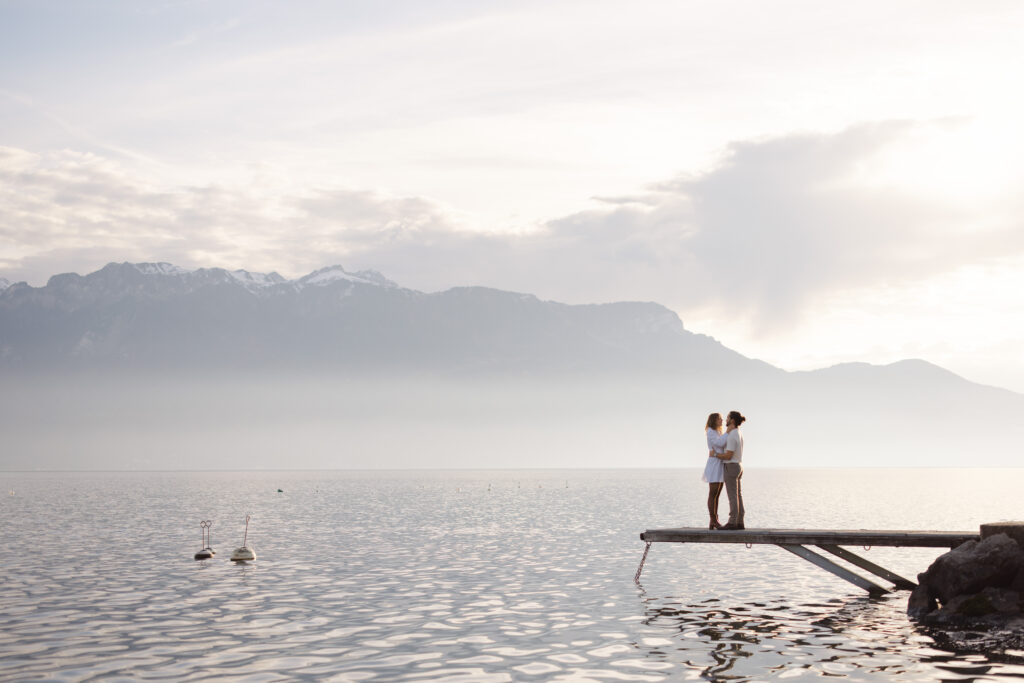 Couple standing on wooden jetty over Lake Geneva with Swiss Alps in background