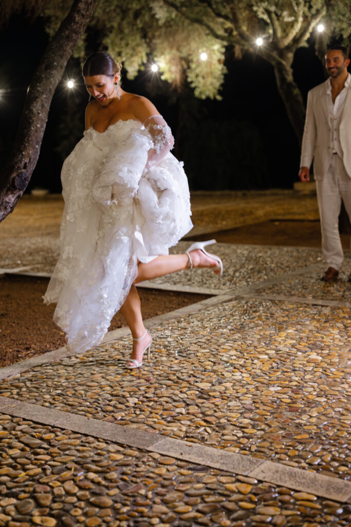 Bride jumping joyfully on wet cobblestones at night, rainy wedding Son Donblon Mallorca